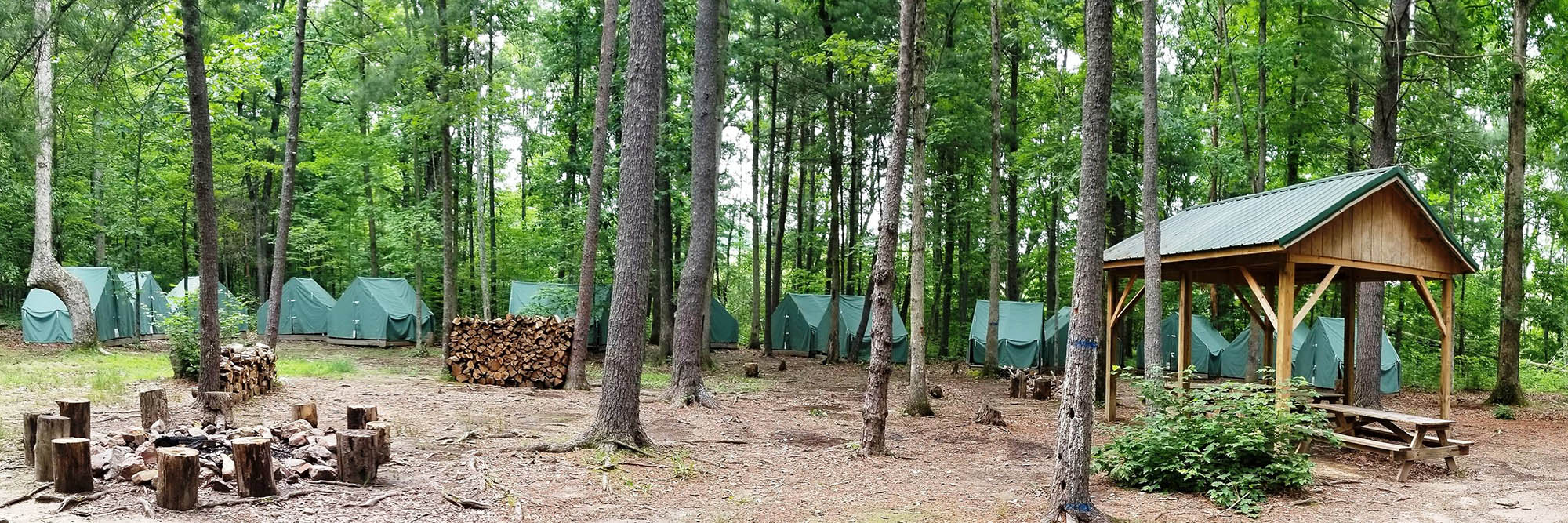 A typical campsite at Camp Shenandoah, with a fire ring, a covered picnic table, and a group of canvas tents